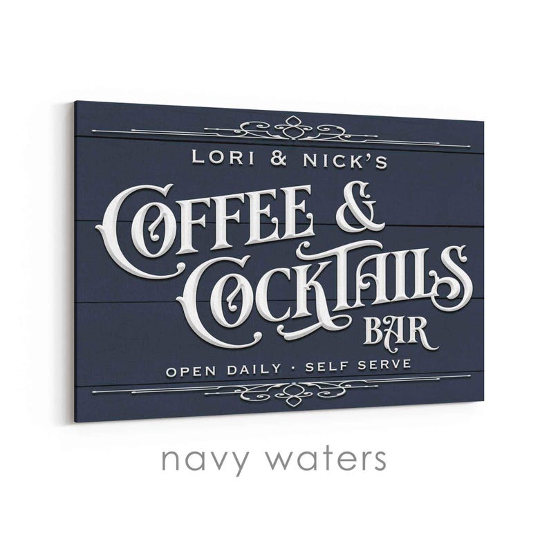 May include: Navy blue wooden sign with white lettering that reads "Lori & Nick's Coffee & Cocktails Bar." The sign also includes the text "Open Daily - Self Serve" and decorative flourishes.