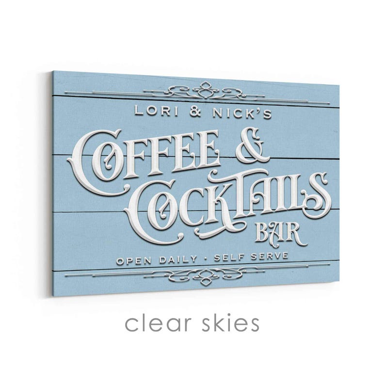 May include: A light blue wooden sign with white lettering that reads "LORI & NICK'S COFFEE & COCKTAILS BAR." The sign has a distressed, rustic look with decorative flourishes and the words "OPEN DAILY - SELF SERVE."