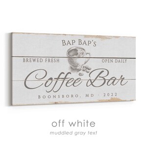 Pode incluir: Placa de madeira branca suja com texto cinza turvo. A placa diz "Bap Bap's Coffee Bar" com uma ilustra&ccedil;&atilde;o de x&iacute;cara de caf&eacute;. O texto adicional inclui "Brewed Fresh", "Open Daily", "Boonsboro, MD 2022".