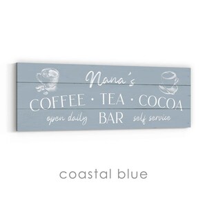 May include: A coastal blue wooden sign with white text. The sign reads "Nana's COFFEE &bull; TEA &bull; COCOA open daily BAR self service." It features illustrations of coffee cups.