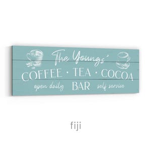 May include: A rectangular, pale blue wooden sign with white text and illustrations. The sign reads "The Youngs' COFFEE &bull; TEA &bull; COCOA BAR open daily self service". The sign has illustrations of coffee cups.