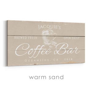 Pode incluir: Uma placa retangular de madeira com um fundo de areia quente. A placa diz "Jacquie's Coffee Bar" em escrita branca, com "Brewed Fresh" e "Open Daily" acima e um gr&aacute;fico de x&iacute;cara de caf&eacute;. O texto "Oceanside, CA 2018" est&aacute; na parte inferior.