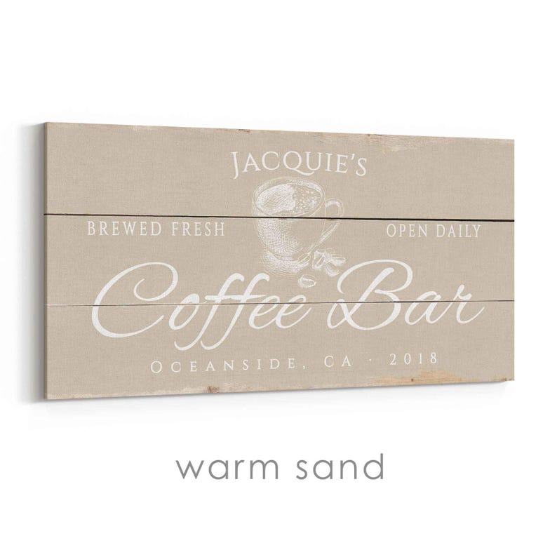 Pode incluir: Uma placa retangular de madeira com um fundo de areia quente. A placa diz "Jacquie's Coffee Bar" em escrita branca, com "Brewed Fresh" e "Open Daily" acima e um gr&aacute;fico de x&iacute;cara de caf&eacute;. O texto "Oceanside, CA 2018" est&aacute; na parte inferior.