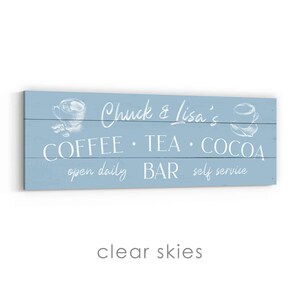 May include: A pale blue wooden sign with white lettering. It reads "Chuck & Lisa's COFFEE &bull; TEA &bull; COCOA BAR open daily self service." There are illustrations of coffee cups.