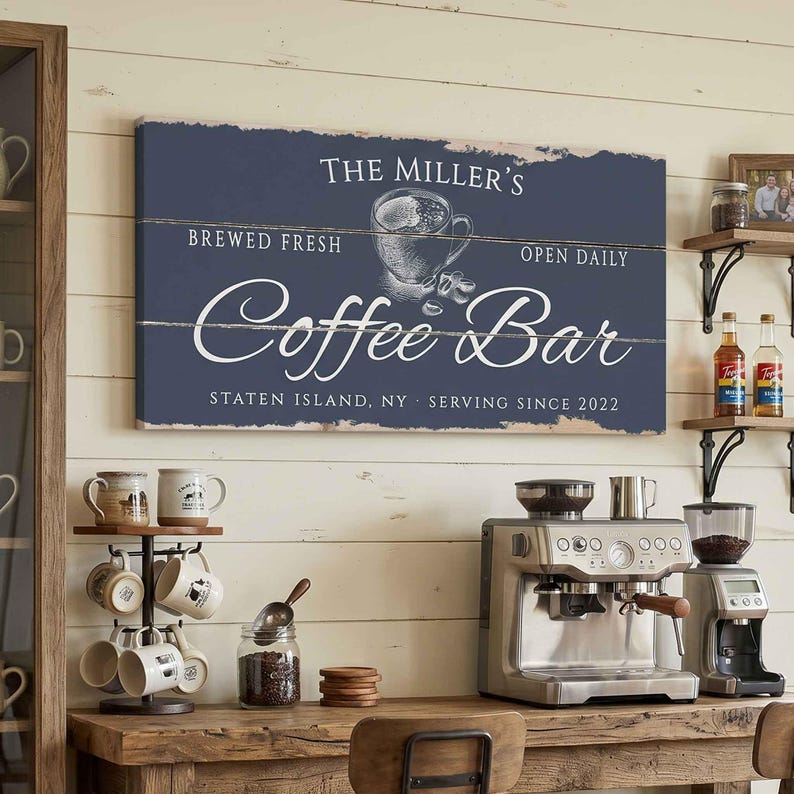 Pode incluir: Uma placa de madeira azul marinho que diz "The Miller's Coffee Bar" com uma ilustra&ccedil;&atilde;o de x&iacute;cara de caf&eacute;. A placa tamb&eacute;m inclui o texto "Brewed Fresh, Open Daily, Serving Since 2022, Staten Island, NY". A placa &eacute; montada em uma parede de madeira branca.