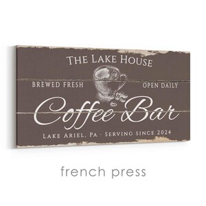 Pode incluir: Uma placa retangular de madeira com fundo marrom e texto branco. A placa diz "THE LAKE HOUSE", "BREWED FRESH", "OPEN DAILY" e "Coffee Bar". Uma ilustra&ccedil;&atilde;o de uma x&iacute;cara de caf&eacute; est&aacute; no centro. O texto "LAKE ARIEL, PA SERVING SINCE 2024" est&aacute; na parte inferior.