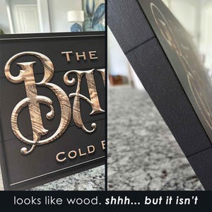 K&ouml;nnte beinhalten: Ein schwarzes Schild mit den Worten "The Barn" in goldenen Buchstaben mit einer Holzmaserung. Das Schild tr&auml;gt au&szlig;erdem den Schriftzug "Cold Fresh" in kleineren goldenen Buchstaben. Das Schild ist aus einem Material gefertigt, das wie Holz aussieht, aber keines ist.