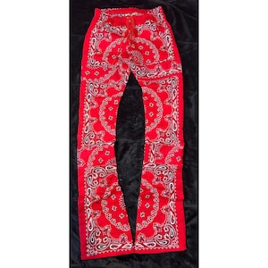 May include: Red bandana-print pants with a drawstring waist. The pants feature a classic paisley pattern in white and black, creating a bold contrast against the vibrant red fabric. The pants have a relaxed fit.