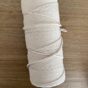May include: A roll of natural cotton rope, perfect for crafting projects. The rope is tightly wound and has a natural, off-white color.