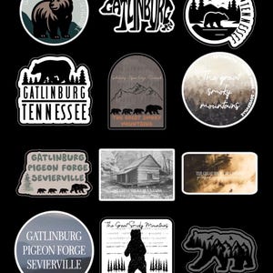 May include: A collection of stickers featuring designs related to Gatlinburg, Tennessee, and the Great Smoky Mountains. The stickers include images of bears, mountain landscapes, and text such as "Gatlinburg" and "The Great Smoky Mountains."
