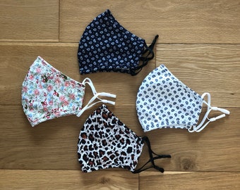 May include: Four fabric face masks with different patterns. One mask is white with a blue paisley pattern, one is white with a red and pink floral pattern, one is white with a black paisley pattern, and one is brown with a black leopard print.