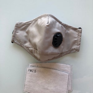 May include: A beige face mask with a black valve and two beige PM2.5 filters.