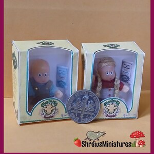 May include: Two Cabbage Patch Kids dolls in their original boxes. The dolls are dressed in vintage clothing and are holding books. The boxes are yellow with green trim and feature the Cabbage Patch Kids logo.