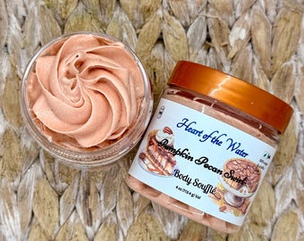 May include: A clear plastic jar of peach-coloured body soufflé with a copper-coloured lid. The label reads Heart of the Water Pumpkin Pecan Swirl 4 oz (113.4 g) Vol, featuring illustrations of a pumpkin pecan pie and a slice of pie on a pedestal.