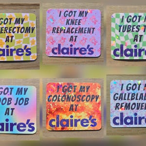 May include: A collection of six square stickers with the text "I GOT MY... AT claire's". The stickers have different backgrounds and text, including "Hysterectomy", "Knee Replacement", "Tubes Tied", "Boob Job", "Colonoscopy", and "Gallbladder Removed".
