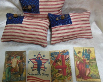 May include: Three small red, white, and blue American flag pillows with blue stars and a bell on each.  Four vintage postcards with patriotic themes, including "Veterans Day", "July 4th", and "Memorial Day".
