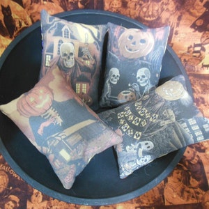 May include: Four Halloween-themed fabric pillow covers with various designs, including a pumpkin, a skeleton, and a haunted house. The pillow covers are arranged in a black bowl.