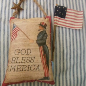 May include: A handmade patriotic pillow with a red, white, and blue American flag design. The pillow features a vintage illustration of a man in a tricorn hat holding a flag and the text "God Bless America".