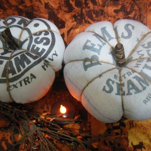 May include: Two white fabric pumpkins decorated with brown twine and black text. The text on the pumpkins reads "Seamless Extra Heavy" and "Seamless Extra Heavy Reg. U.S. Pat. Off. 15".