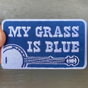 May include: Blue embroidered patch with white text that reads "My Grass Is Blue" and a white banjo illustration.