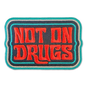 May include: A black and turquoise embroidered patch with the text "NOT ON DRUGS" in red.