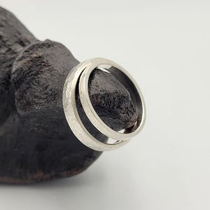 Pode incluir: Um anel de metal prateado com um padr&atilde;o de superf&iacute;cie texturizado e gravado na banda externa. O anel possui uma banda interna lisa e polida e uma forma circular consistente, apresentada numa vista clara contra um fundo neutro.