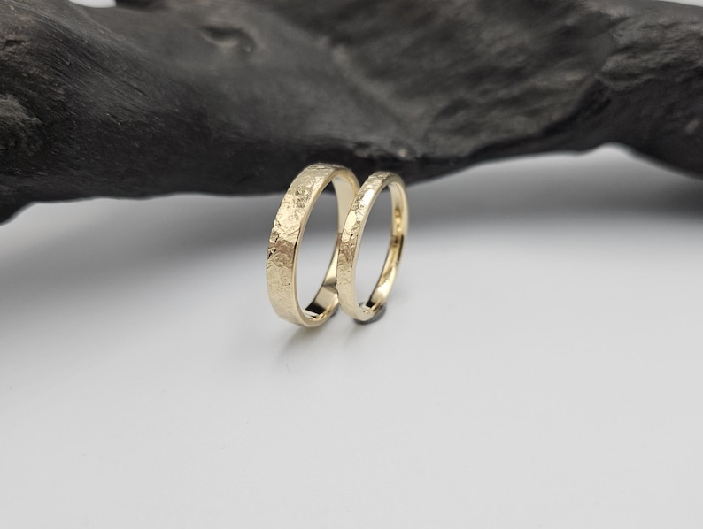 Puede incluir: Dos anillos de oro con un acabado de superficie texturizado y martillado. Los anillos son bandas circulares con un interior pulido y una textura exterior rugosa e irregular que capta la luz. Los dos anillos est&aacute;n colocados en posici&oacute;n vertical.