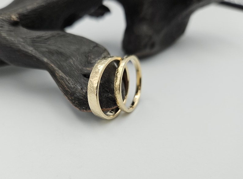 May include: Two gold wedding bands with a hammered texture. The bands are stacked on top of each other.