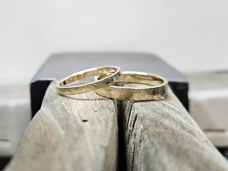Puede incluir: Dos anillos de oro con un acabado texturizado y martillado. Los anillos son bandas circulares con un brillo amarillo met&aacute;lico y un patr&oacute;n de superficie rugoso e irregular. Las bandas est&aacute;n colocadas juntas, mostrando un dise&ntilde;o consistente.
