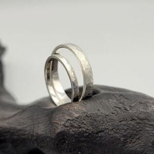 Pode incluir: Dois an&eacute;is de tom prateado com um acabamento texturizado e martelado. Os an&eacute;is apresentam um design de banda circular fina com uma superf&iacute;cie met&aacute;lica mate. A superf&iacute;cie exterior de cada anel exibe um padr&atilde;o irregular e consistente.