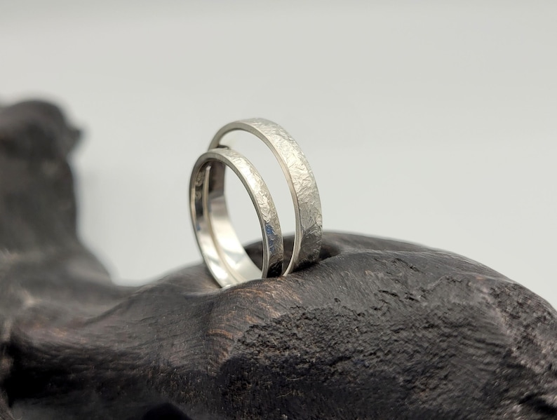 Pode incluir: Dois an&eacute;is de tom prateado com um acabamento texturizado e martelado. Os an&eacute;is apresentam um design de banda circular fina com uma superf&iacute;cie met&aacute;lica mate. A superf&iacute;cie exterior de cada anel exibe um padr&atilde;o irregular e consistente.
