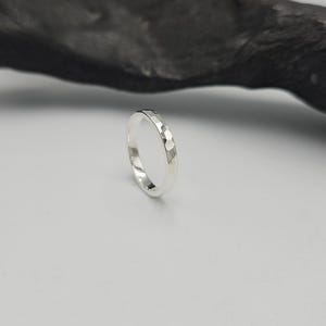 May include: A silver ring with a faceted, hammered texture on the outer surface. The band has a polished, reflective finish that catches the light, creating a series of small, geometric, multi-sided indentations around the entire circumference.
