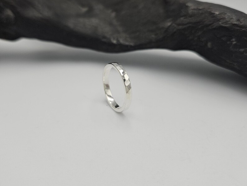 May include: A silver ring with a faceted, hammered texture on the outer surface. The band has a polished, reflective finish that catches the light, creating a series of small, geometric, multi-sided indentations around the entire circumference.