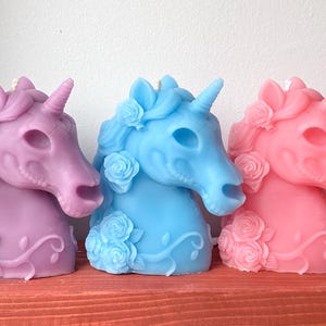 May include: Three unicorn head candles, one purple, one light blue, and one pink. Each candle has a detailed design of roses and vines.