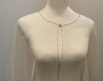 May include: A white tulle bridal cape with a beaded trim and a silver chain tie. The cape is on a white mannequin.