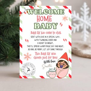 Może przedstawiać: Świąteczna kartka z czerwono-zieloną obwódką. Na kartce widnieje napis "WELCOME HOME BABY" oraz wiersz o baby elfie. Zawiera również ilustrację baby elfa owiniętego w różowy kocyk.