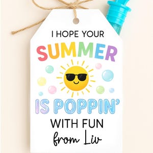 May include: A white gift tag with the text "I HOPE YOUR SUMMER IS POPPIN' WITH FUN from Liv" and a cartoon sun wearing sunglasses. The tag is tied with twine and includes a blue bubble wand.