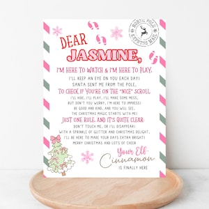 May include: A Christmas letter addressed to "Jasmine" with festive decorations. The letter includes text about an elf named Cinnamon, Santa, and Christmas cheer. The design features pink, green, and white colours.