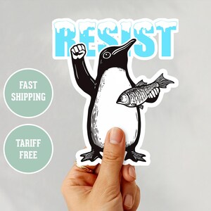 Könnte beinhalten: Schwarz-weiß-Illustration eines Pinguins mit erhobener Faust, der einen Fisch hält. Der Pinguin steht auf einem weißen Hintergrund mit dem Wort "RESIST" in blauen Buchstaben darüber.