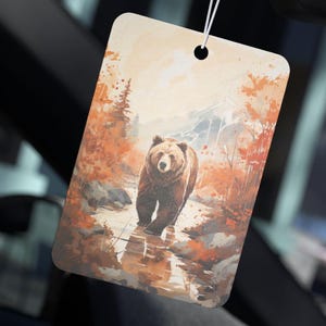 May include: A brown bear walks through a stream in a forest setting. The bear is walking towards the viewer. The background is a watercolor painting of trees and mountains.