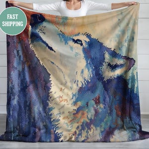Op de afbeelding: Een grote, zachte deken met een gedetailleerde afbeelding van een huilende wolf. Het kunstwerk gebruikt tinten blauw, wit en bruin om een ​​gestructureerd, artistiek effect te creëren. De deken wordt omhoog gehouden en toont het volledige ontwerp.