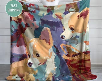 Könnte beinhalten: Eine farbenfrohe Decke mit einem abstrakten Gemälde von Corgi-Hunden. Das Kunstwerk verwendet eine Palette aus Orange, Weiß, Blau und Lila. Die Decke wird von einer Person präsentiert, die das Design zeigt.