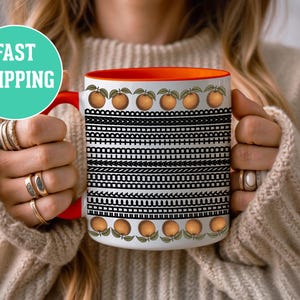 Puede incluir: Taza de cerámica blanca con asa e interior rojos, con un patrón geométrico en blanco y negro e ilustraciones de naranjas. La taza tiene el texto "FAST SHIPPING" en un círculo turquesa.