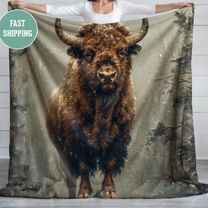 May include: A brown and white bison stands in a snowy forest. The bison is looking directly at the camera. The background is a blurry image of trees and snow.