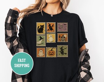 Puede incluir: Camiseta negra con una serie de diseños de sellos postales con temática de Halloween. Los sellos representan un gato negro, una bruja, un esqueleto, un fantasma, una casa embrujada y una calabaza. La camiseta tiene una estética retro.