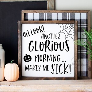 May include: A white wooden sign with black text that reads "Oh look! Another glorious morning... makes me sick!"  The sign has a black spider web and a black pumpkin face graphic. The sign is sitting on a shelf with a white coffee jar, a small orange pumpkin, and a potted green plant.