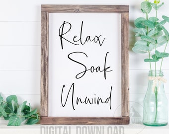 Może przedstawiać: Biały znak w ramie z napisem "Relax Soak Unwind" w czarnym, ozdobnym piśmie. Znak stoi na białej półce z wazą z zielonymi gałązkami eukaliptusa.