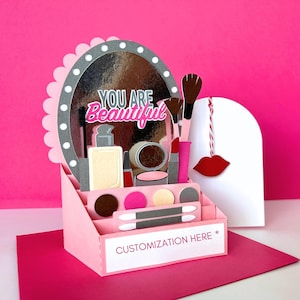 May include: A pink papercraft makeup display with a mirror, makeup brushes, and lip-shaped decoration. The mirror has the text "YOU ARE Beautiful". The display includes a section for customization.