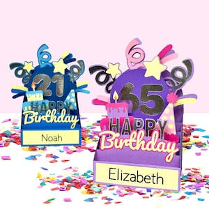 May include: Two decorative birthday cards. One is blue with the number 21, the other is purple with the number 35. Both feature a cake, party hat, and the words "Happy Birthday". The names "Noah" and "Elizabeth" are displayed on the cards.