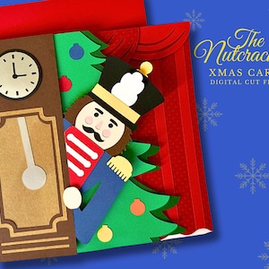 May include: A Christmas card with a paper cutout design featuring a nutcracker soldier, a clock, and a Christmas tree. The card has the text "The Nutcracker XMAS CARD DIGITAL CUT FILE" on a blue background with snowflakes.
